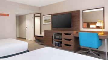 Une chambre d’hôtel avec deux lits, un bureau avec un ordinateur, une télévision et un four à micro-ondes.