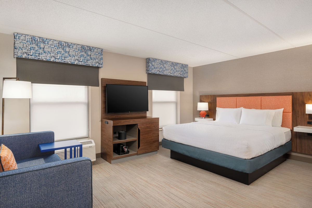 A hotel room with a bed, a TV, a sofa, and a desk with a lamp.