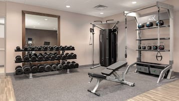 Un gimnasio con equipo de levantamiento de pesas, mancuernas y una banca.