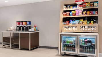 A self-service beverage station with hot, decaf, light roast, and dark roast options, a snack shelf with various brands, and a refrigerated drink cooler.