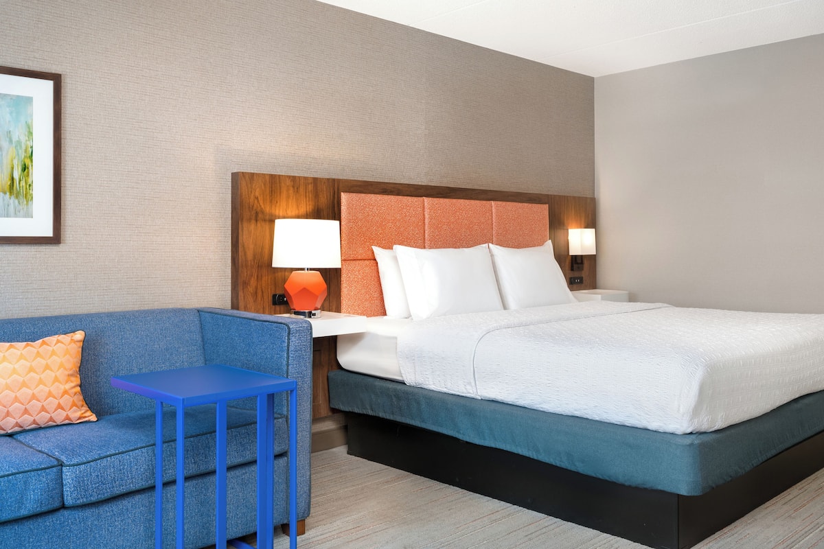 A hotel room with a bed, a blue sofa, a small table, and two bedside lamps.