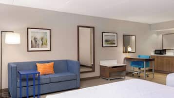 Ein Hotelzimmer mit Bett, blauem Sofa, kleinem Tisch, Schreibtisch mit Stuhl, Mikrowelle und Spiegel im Badezimmer.