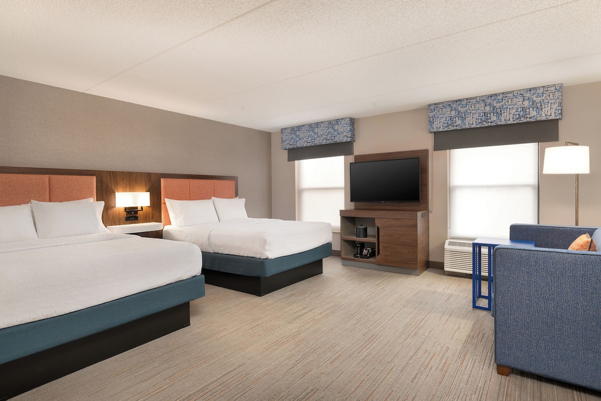 A hotel room with two beds, a TV, a desk, and a sofa.