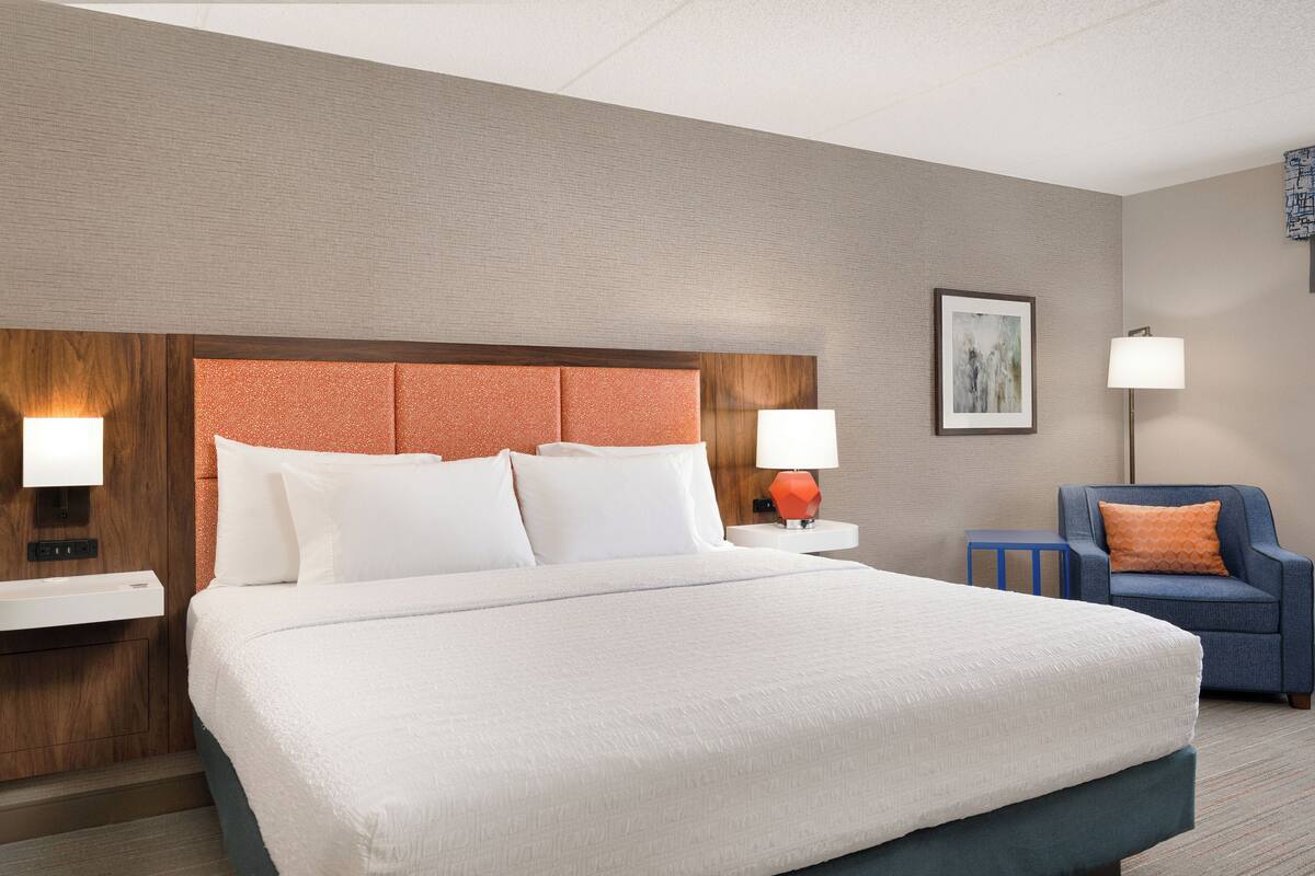A hotel room with a large bed, two bedside tables, a chair, and a wall-mounted lamp.