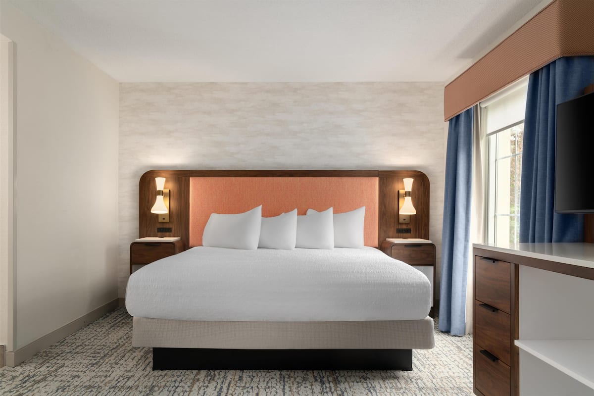 Una habitación de hotel con una cama grande, dos mesitas de noche con lámparas, un aparador y un televisor.