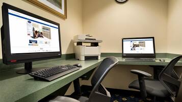 A hotel room with two desktop computers, a printer, and a clock on the wall.