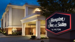 Edifici d'un Hampton Inn & Suites by Hilton amb un cartell ben visible, columnes grans i una entrada ben il·luminada.