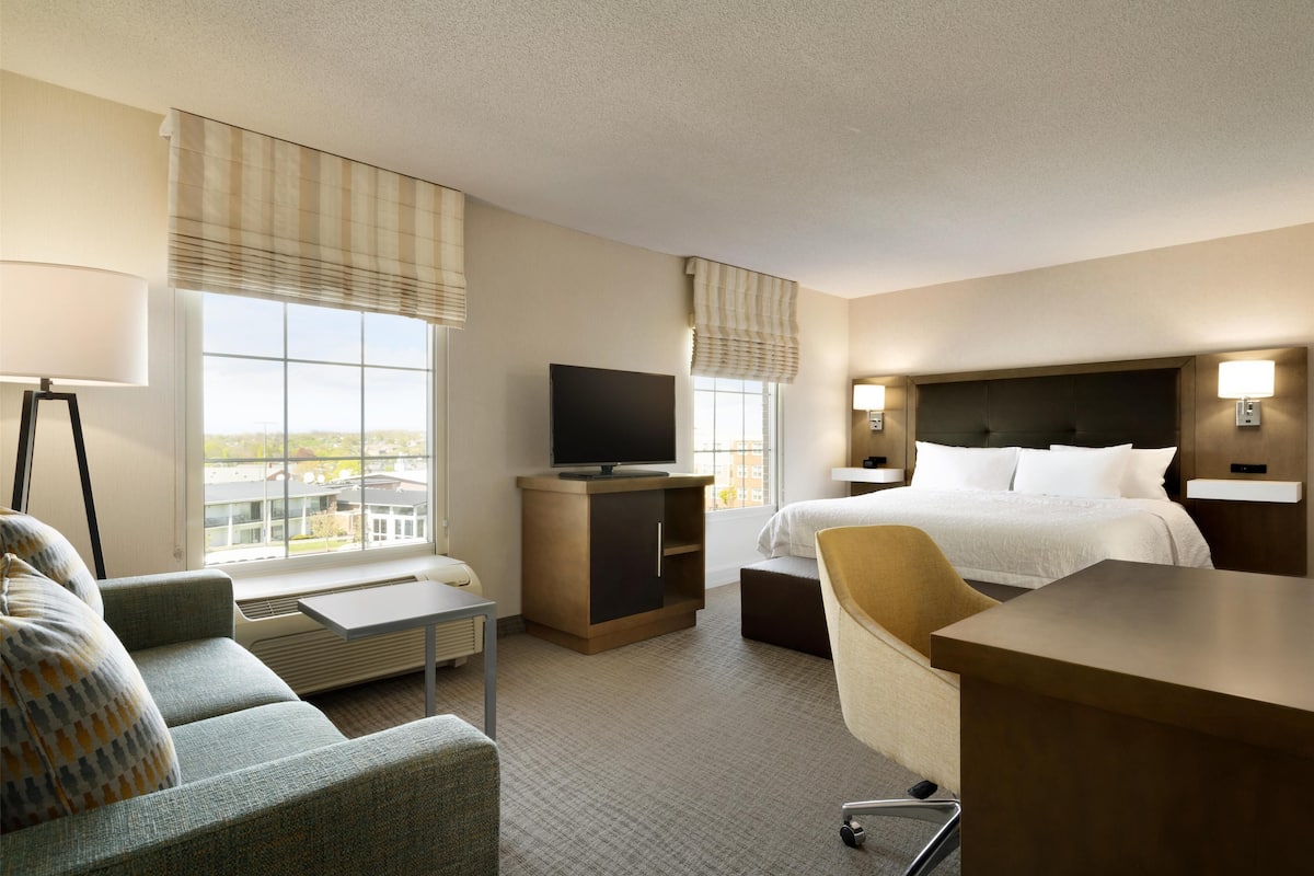 Una habitación de hotel con cama, escritorio, silla, televisor y sofá.