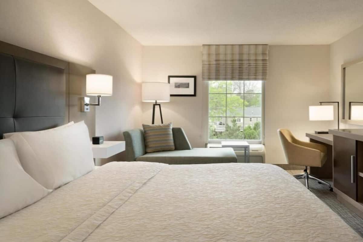Habitación de hotel con dos camas, un escritorio, una silla, una ventana con vistas y una lámpara.