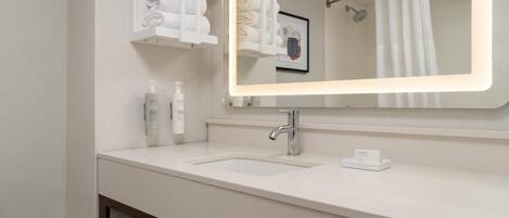 Un baño moderno con un lavabo blanco, un espejo con iluminación integrada, un perchero y un cuadro enmarcado en la pared.