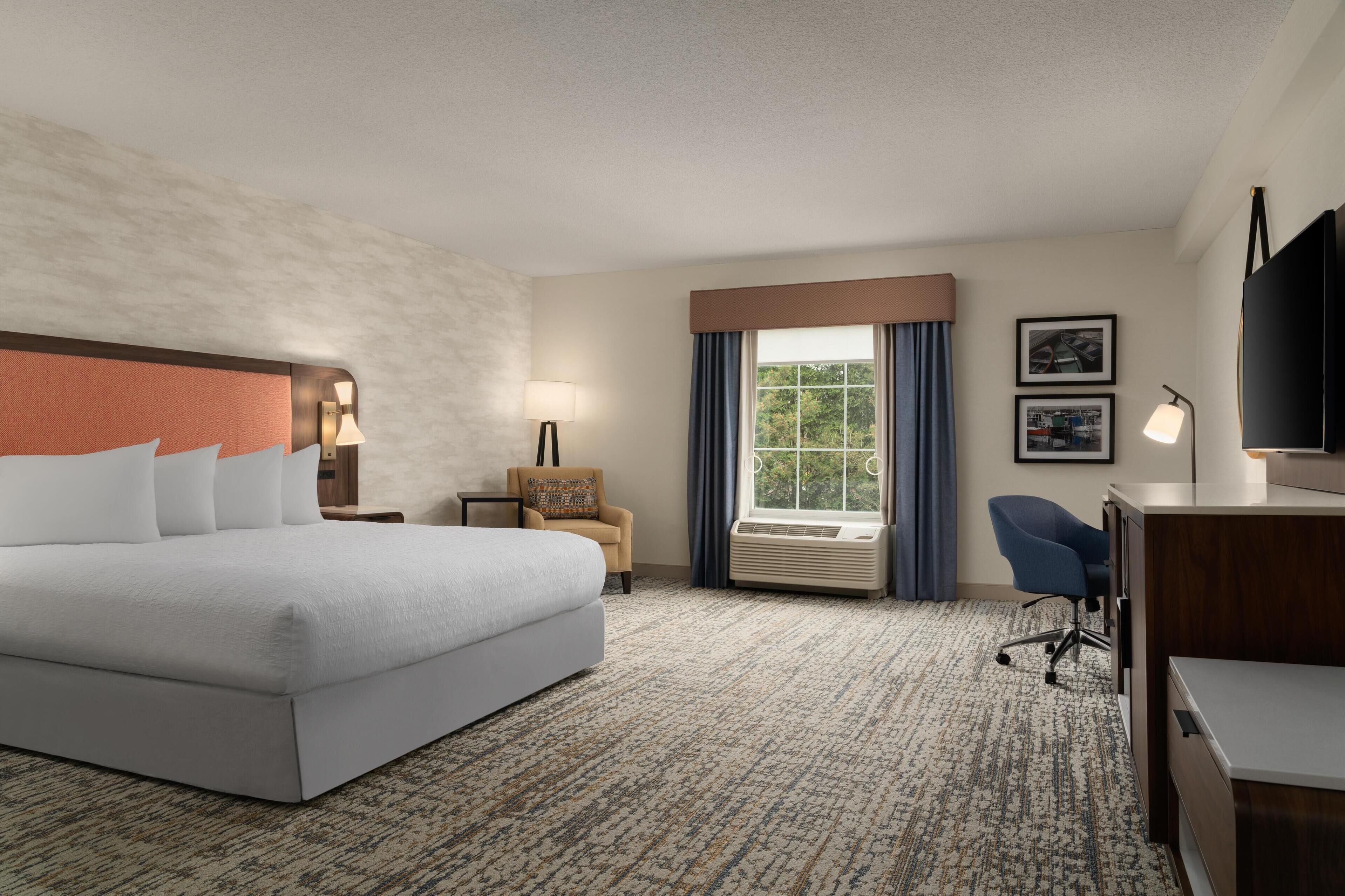 A hotel room with a large bed, a desk, a chair, a TV, and a window with curtains.