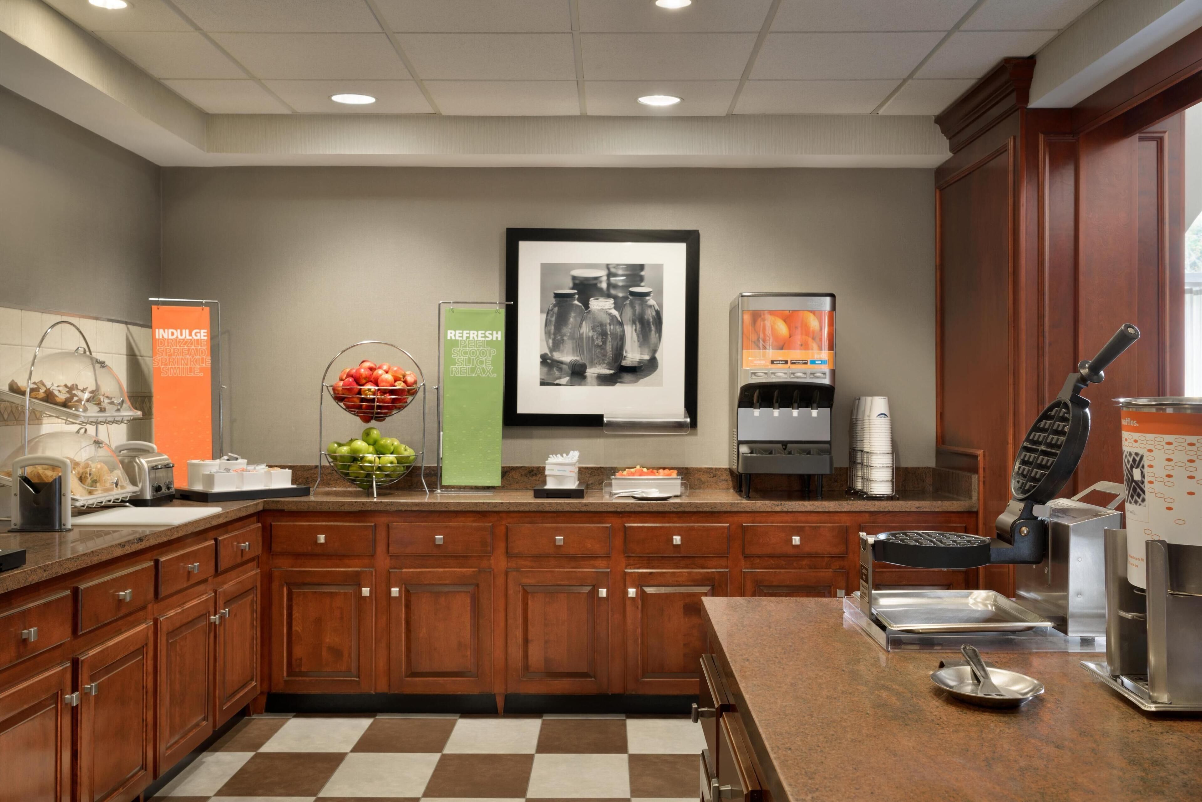 A modern kitchen with wooden cabinets, granite countertops, and various appliances including a waffle maker and coffee machine.
