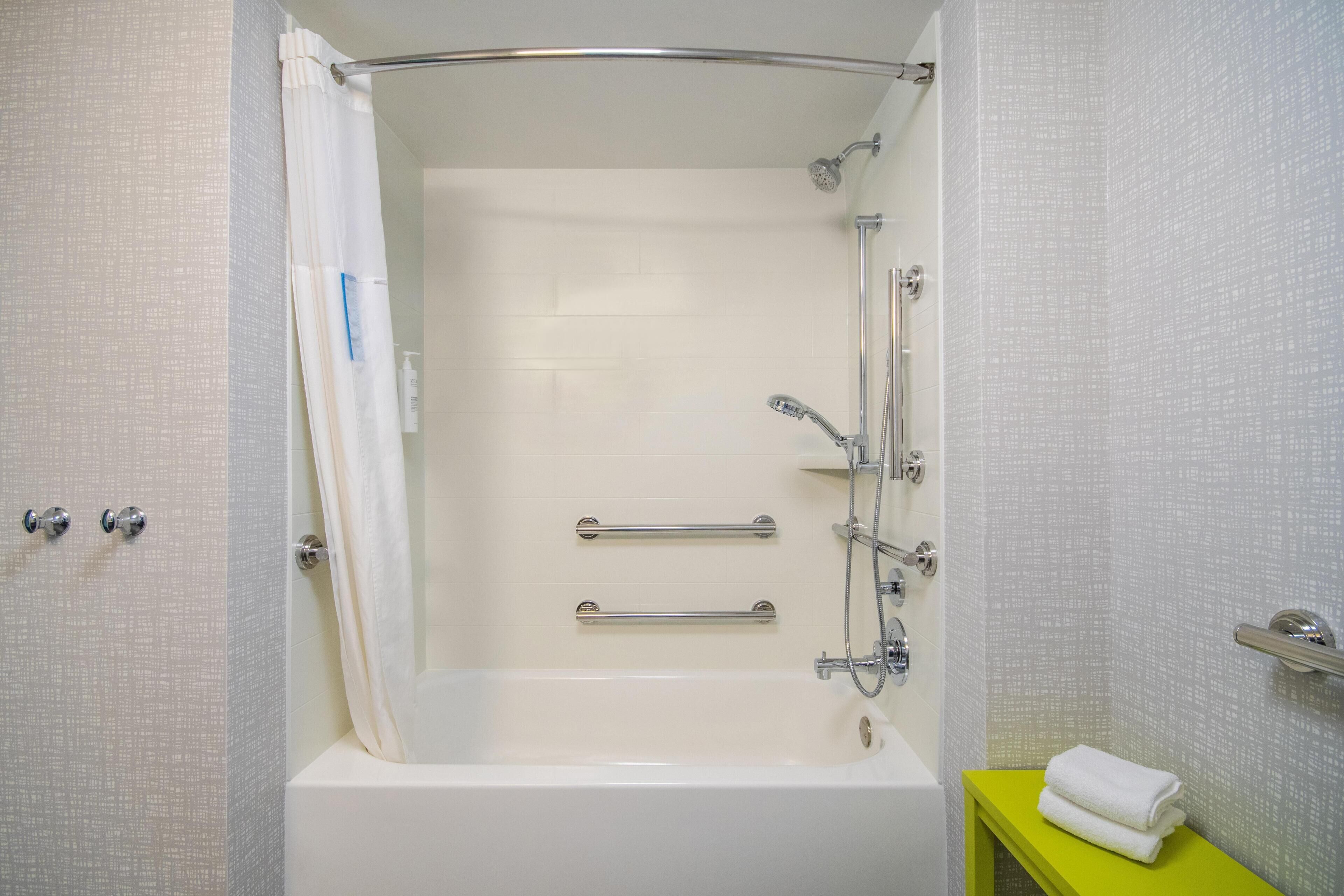 Un baño con bañera, ducha y barras de apoyo.
