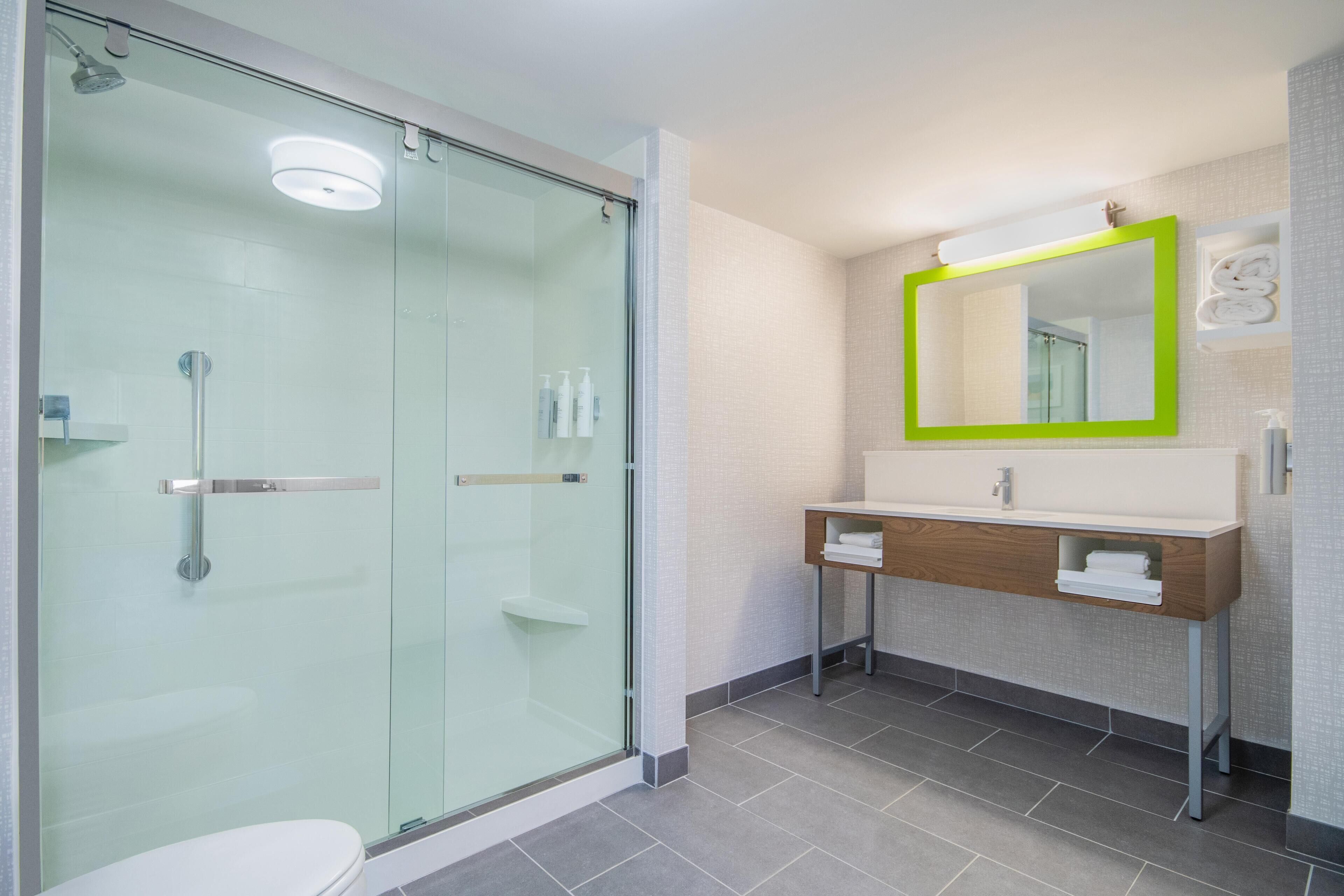 A modern bathroom with a glass shower enclosure, a wooden vanity with a mirror, and a tiled floor.