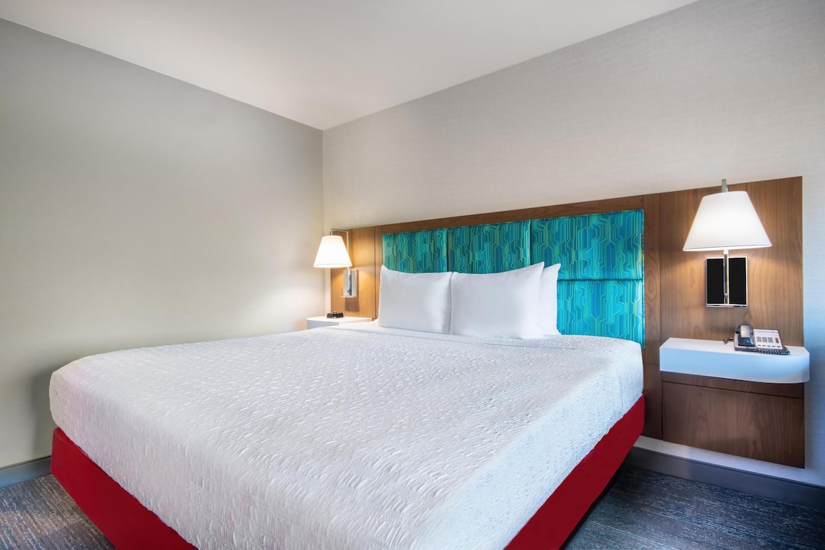 A hotel room with a large bed, two bedside lamps, a wooden headboard, a bedside table with a phone, and a small nightstand.