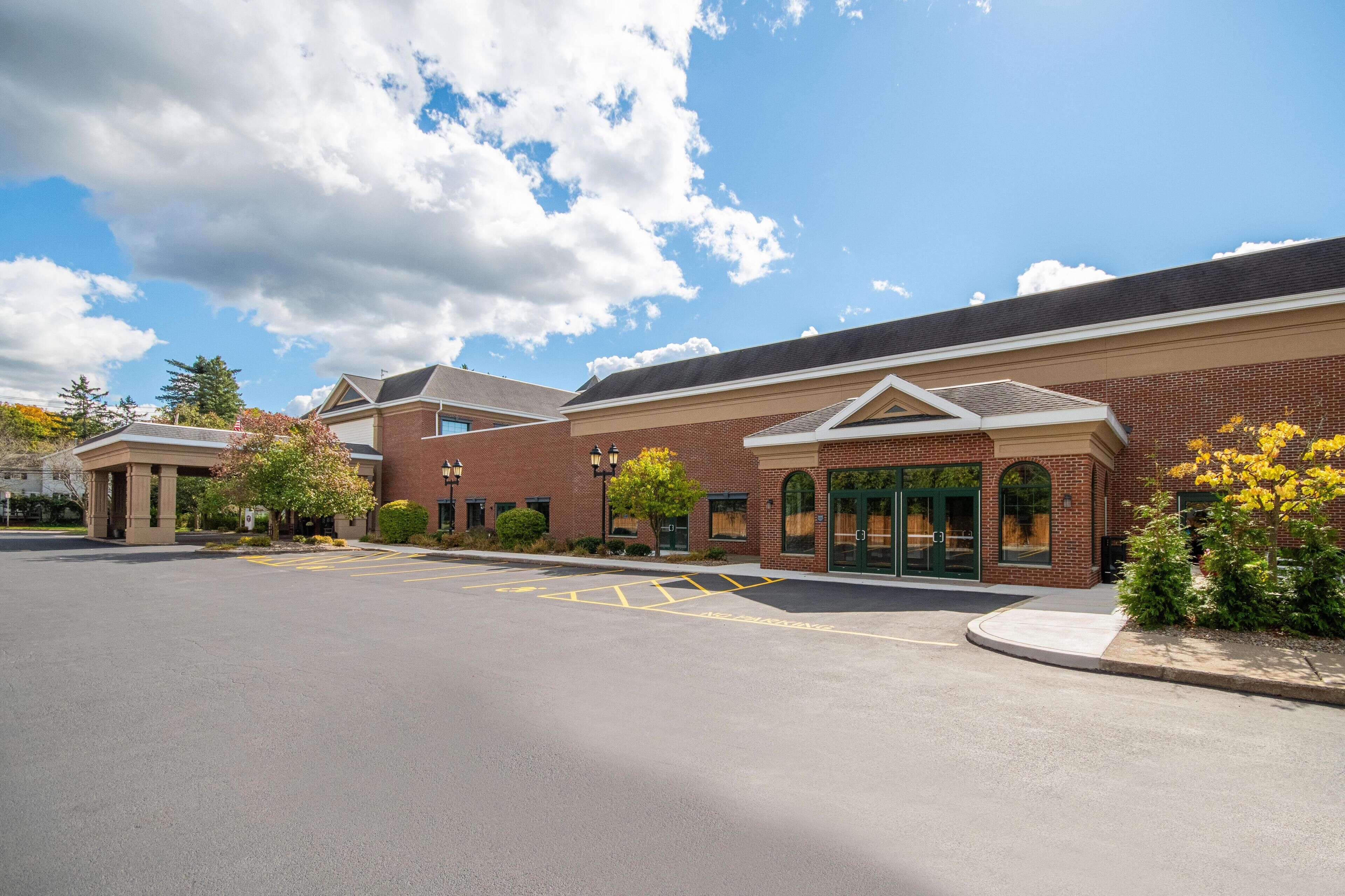 A brick building with a parking lot, a covered entrance, and a small garden area.