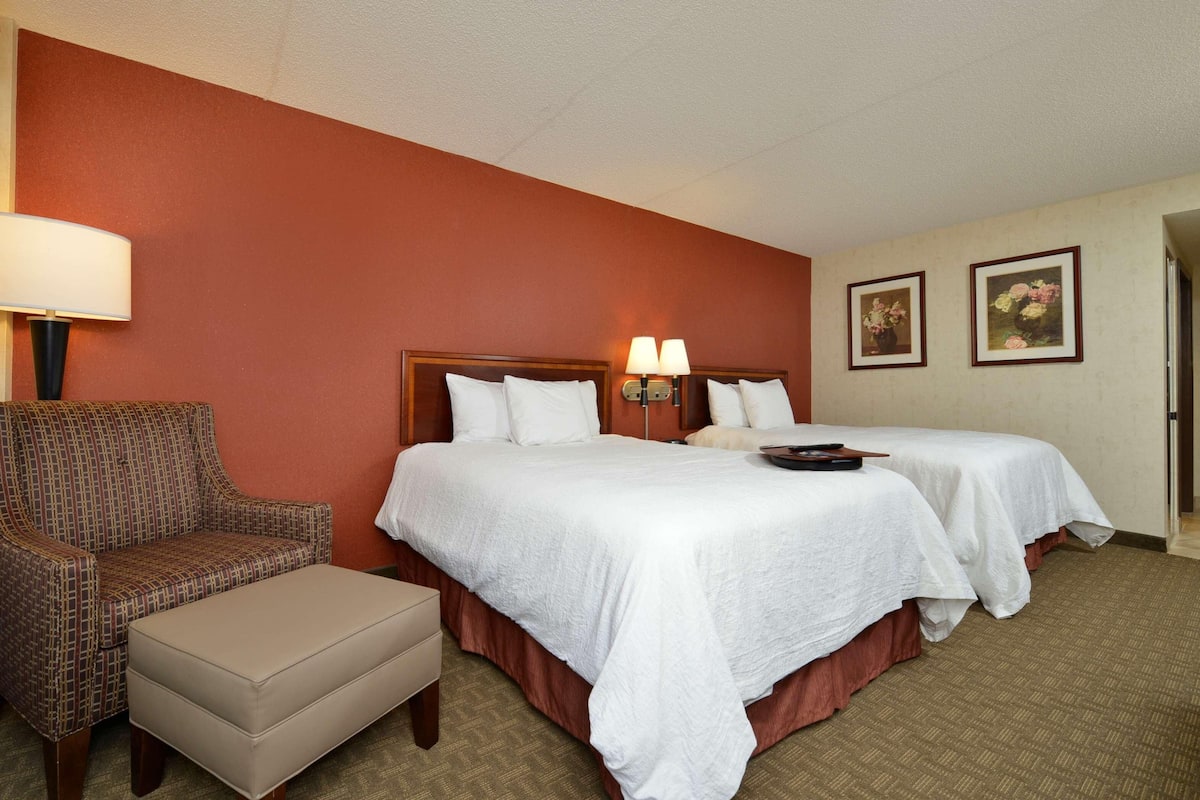A hotel room with two single beds, a chair, and a small table.