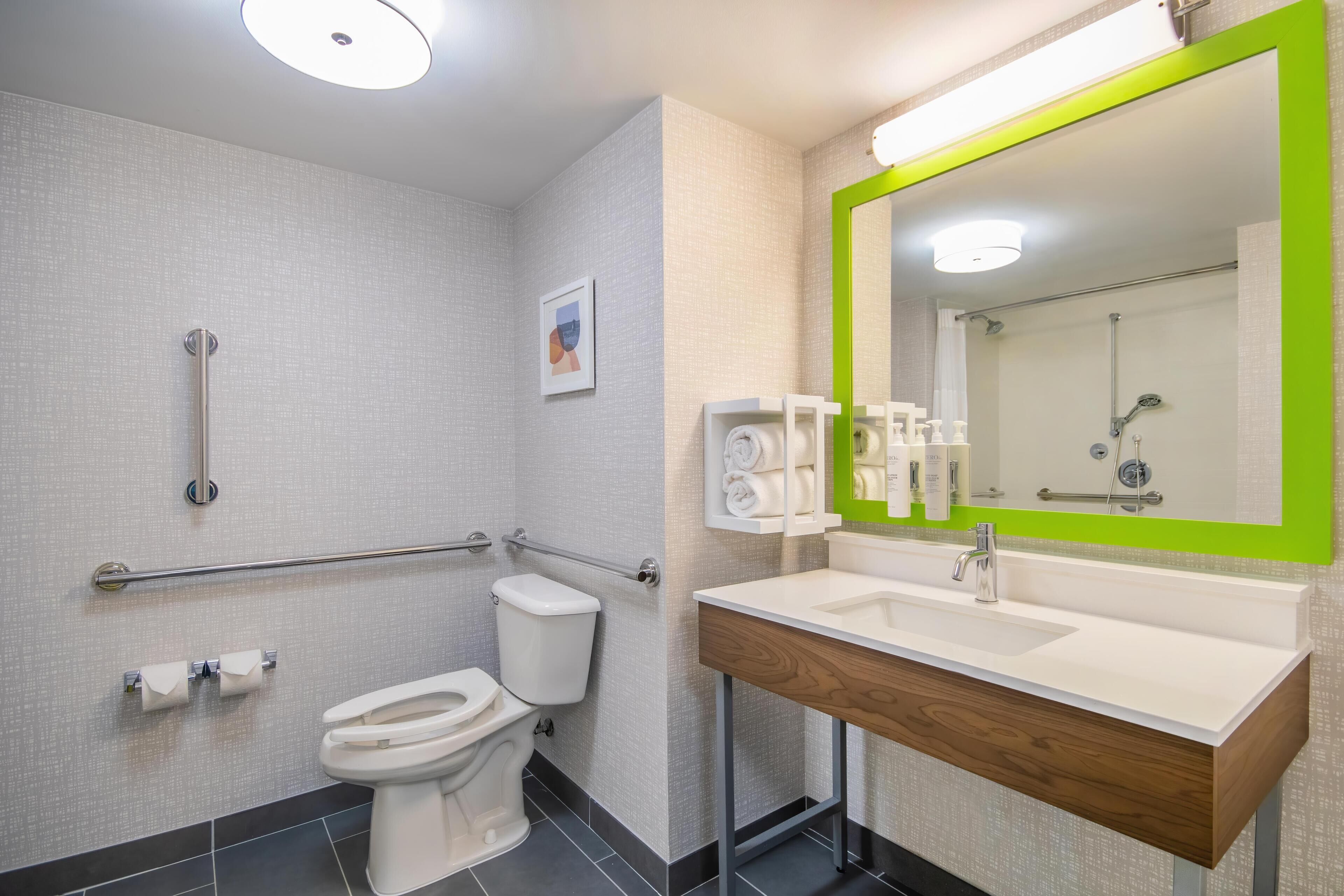 A modern bathroom with a toilet, handrails, a sink, and a mirror.