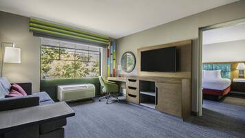 A hotel room with a desk, chair, TV, bed, and a window with a view of trees.
