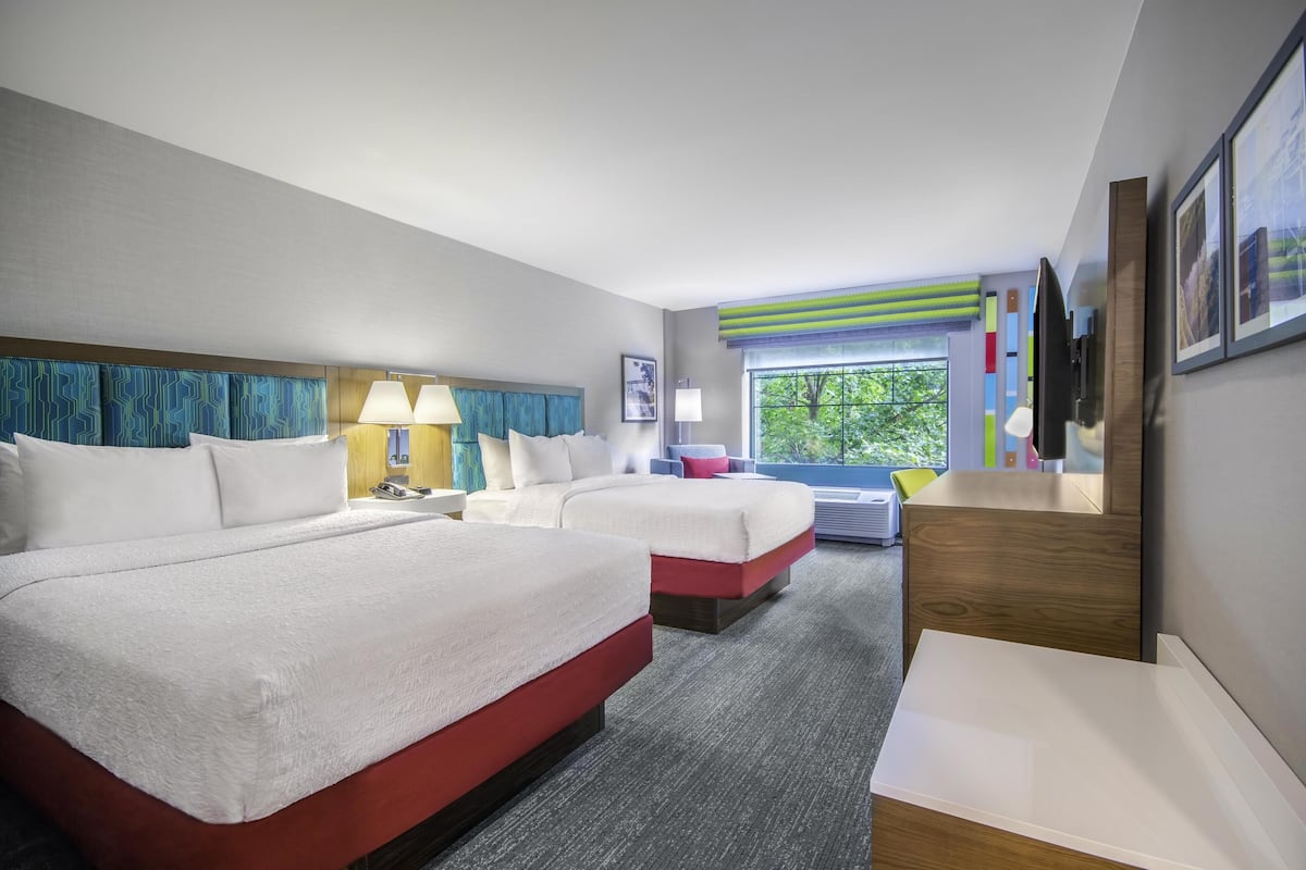 A hotel room with two beds, a desk, a chair, a window with a view, and a TV on the wall.