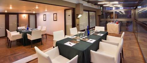 Un salón de conferencias con una larga mesa, sillas blancas y una partición de vidrio.
