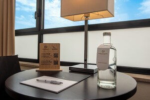 A hotel room with a round table, a lamp, a bottle of water, a pen, and a wooden sign with QR codes.