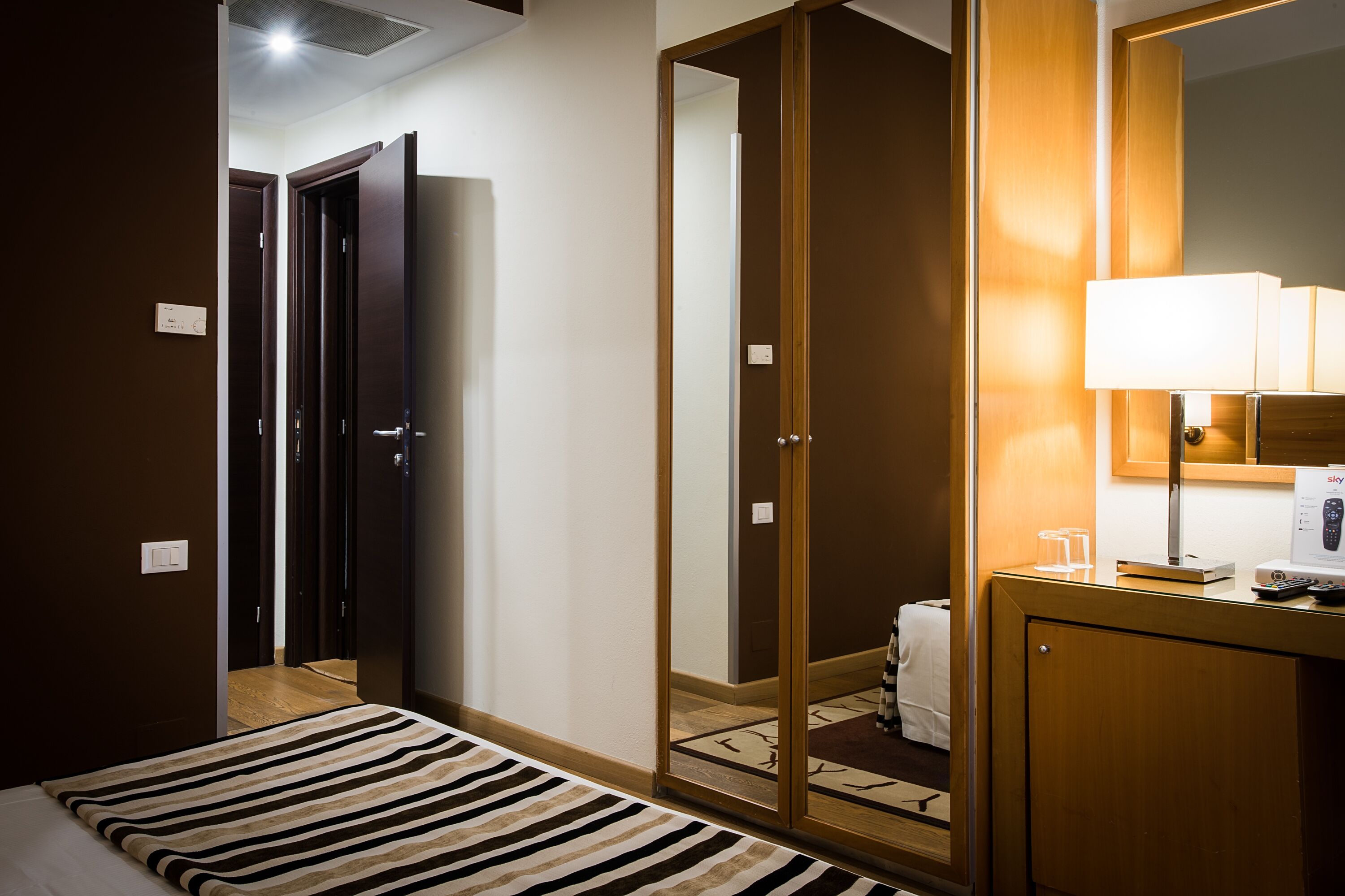 Une chambre d’hôtel comprenant un lit, une table de chevet avec une lampe, un miroir et une armoire.