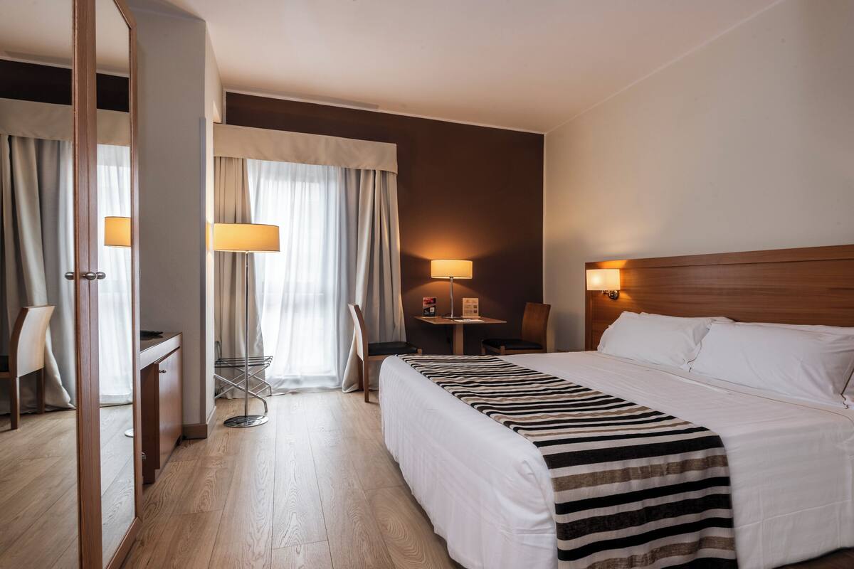 Une chambre d’hôtel avec un grand lit, un bureau, une chaise, une petite table et une lampe.