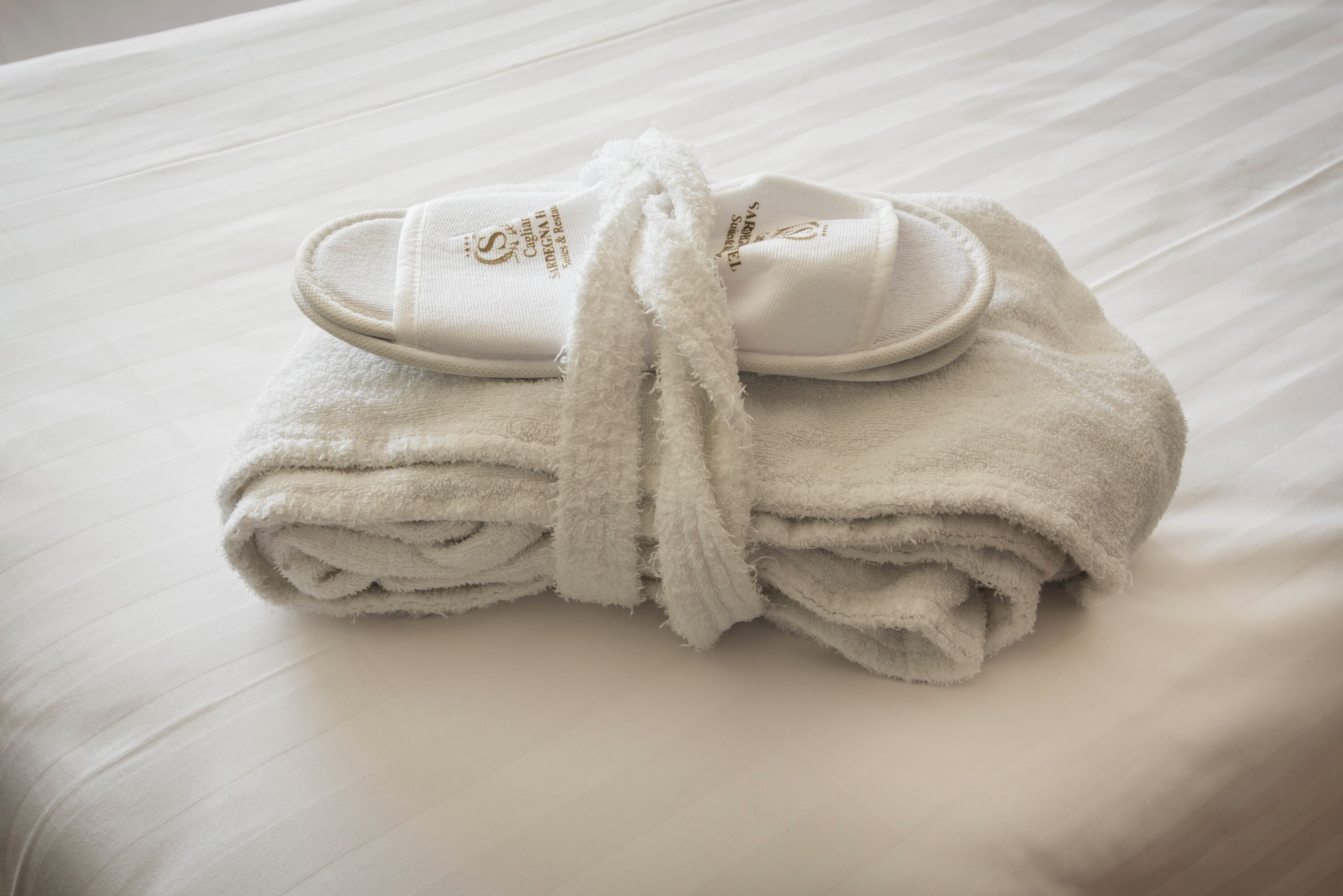 Une serviette blanche soigneusement pliée et un peignoir blanc sont posés sur un lit recouvert de draps blancs.