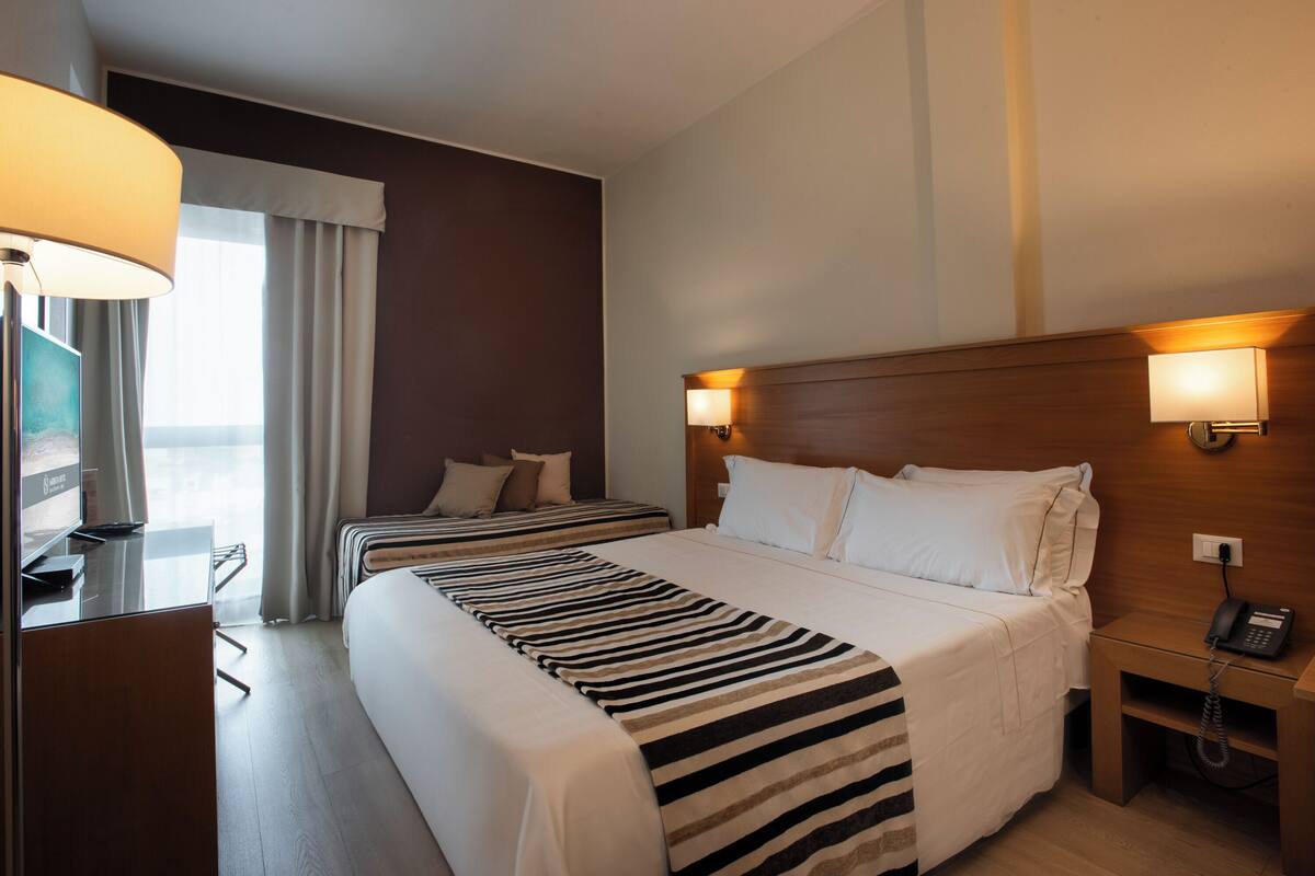 Une chambre d’hôtel avec deux lits, un bureau, une lampe et un téléphone sur une table de chevet.