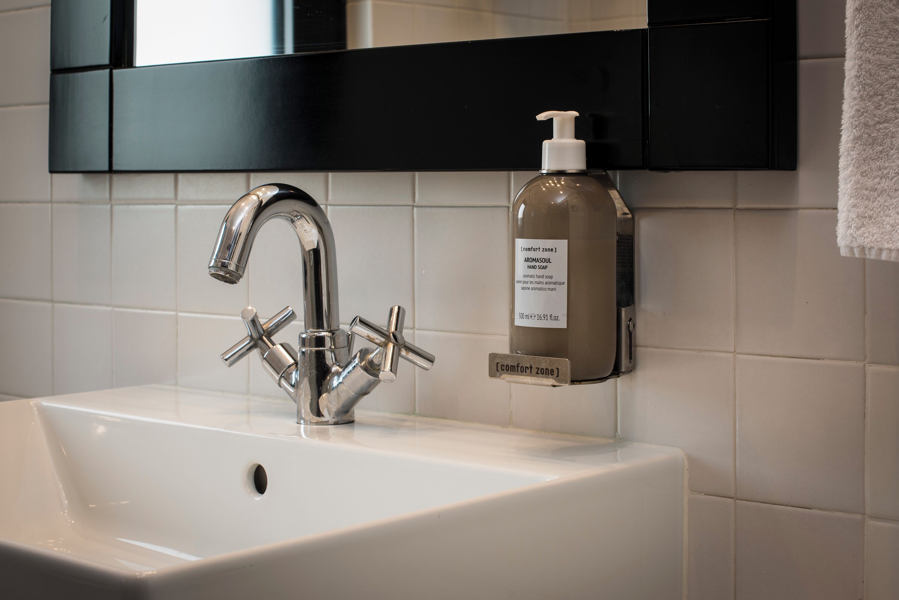 A bathroom sink with a modern faucet, a bottle of hand soap, and a mirror above.