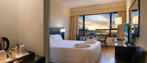 Habitación de hotel con cama, dos sillas, escritorio, televisor y ventana con vista al atardecer.