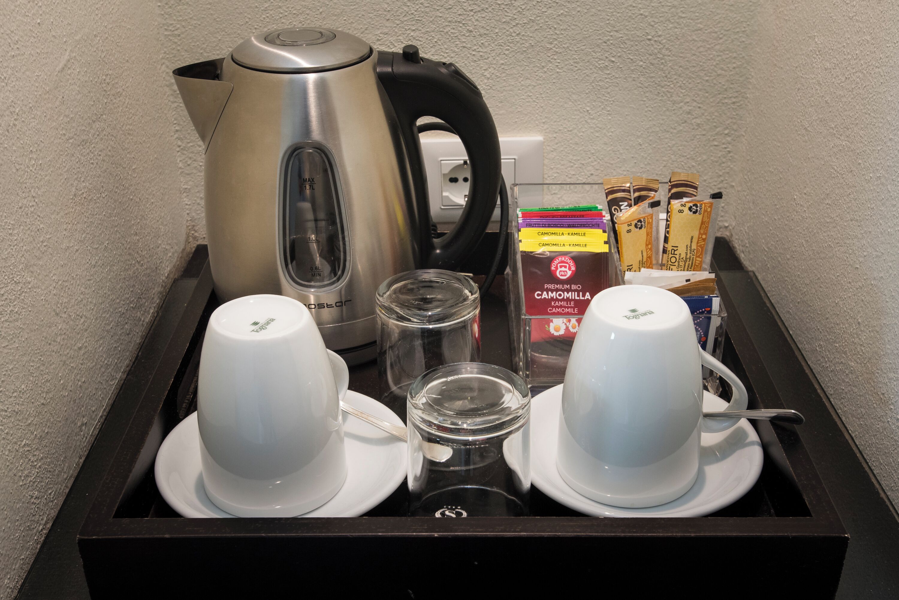 Una bandeja con una tetera, dos tazas, un vaso y sobres de café.