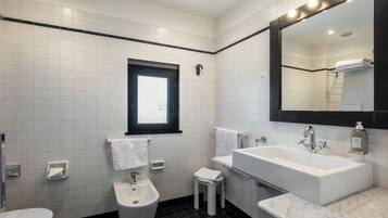 Een moderne badkamer met een grote spiegel, witte tegels, een zwarte vloer, een toilet, een bidet en een wastafel.