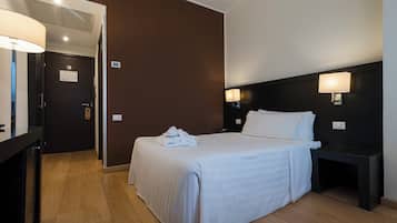 Una habitación de hotel con cama, mesitas de noche, escritorio y lámpara.