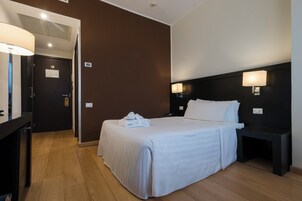 Una habitación de hotel con cama, mesitas de noche, escritorio y lámpara.