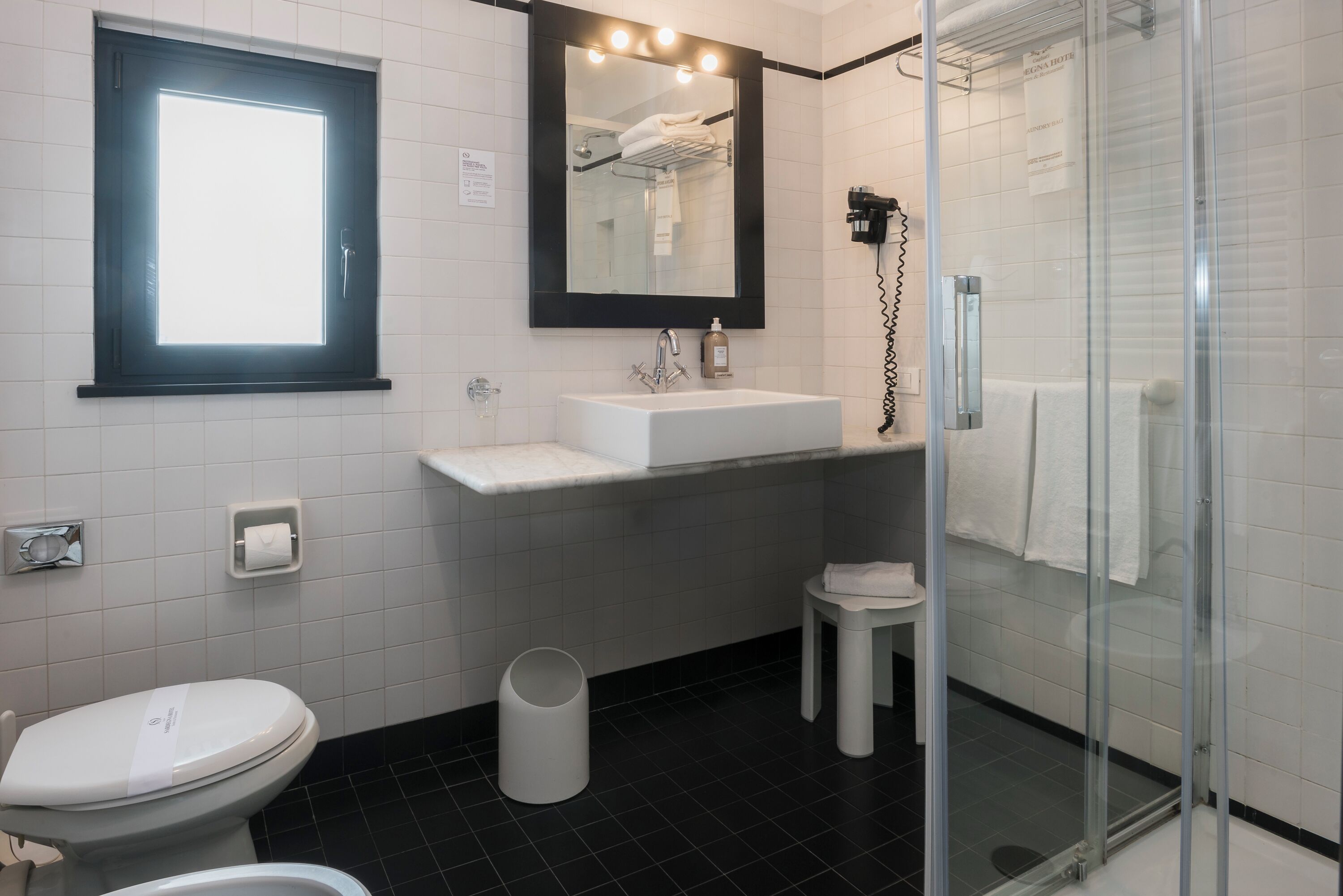 Een moderne badkamer met een witte wastafel, een glazen douchecabine, een toilet en een klein krukje.