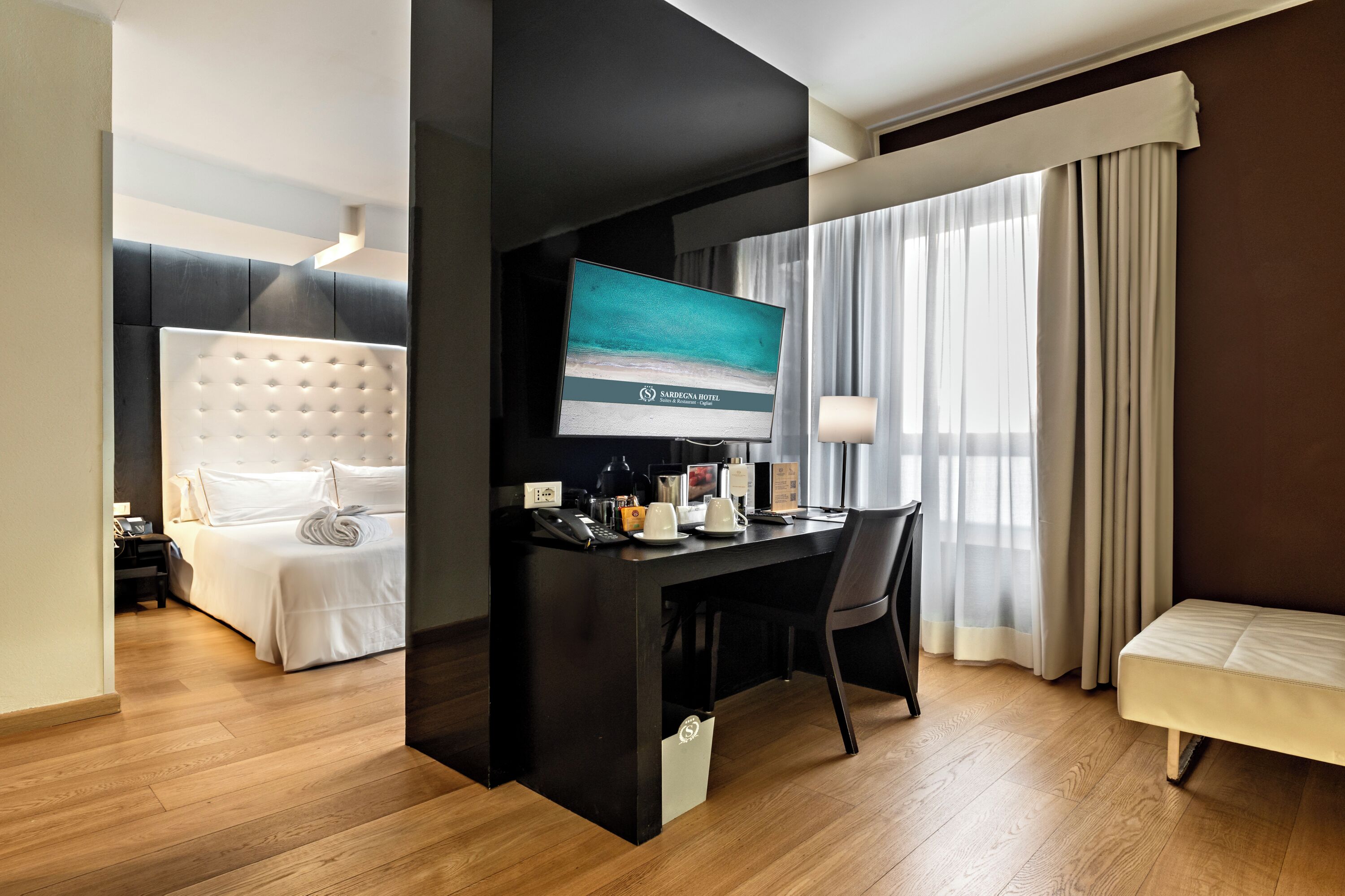 Une chambre d’hôtel avec un lit, un bureau avec un ordinateur, une télévision et une fenêtre avec des rideaux.