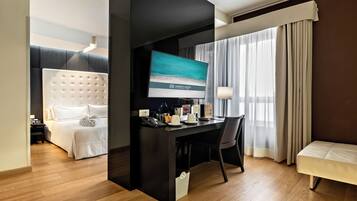 Une chambre d’hôtel avec un lit, un bureau avec un ordinateur, une télévision et une fenêtre avec des rideaux.