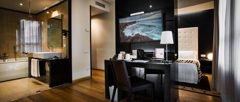 Una habitación de hotel moderna con una cama grande, un escritorio con computadora, televisor y un baño con bañera y ducha.