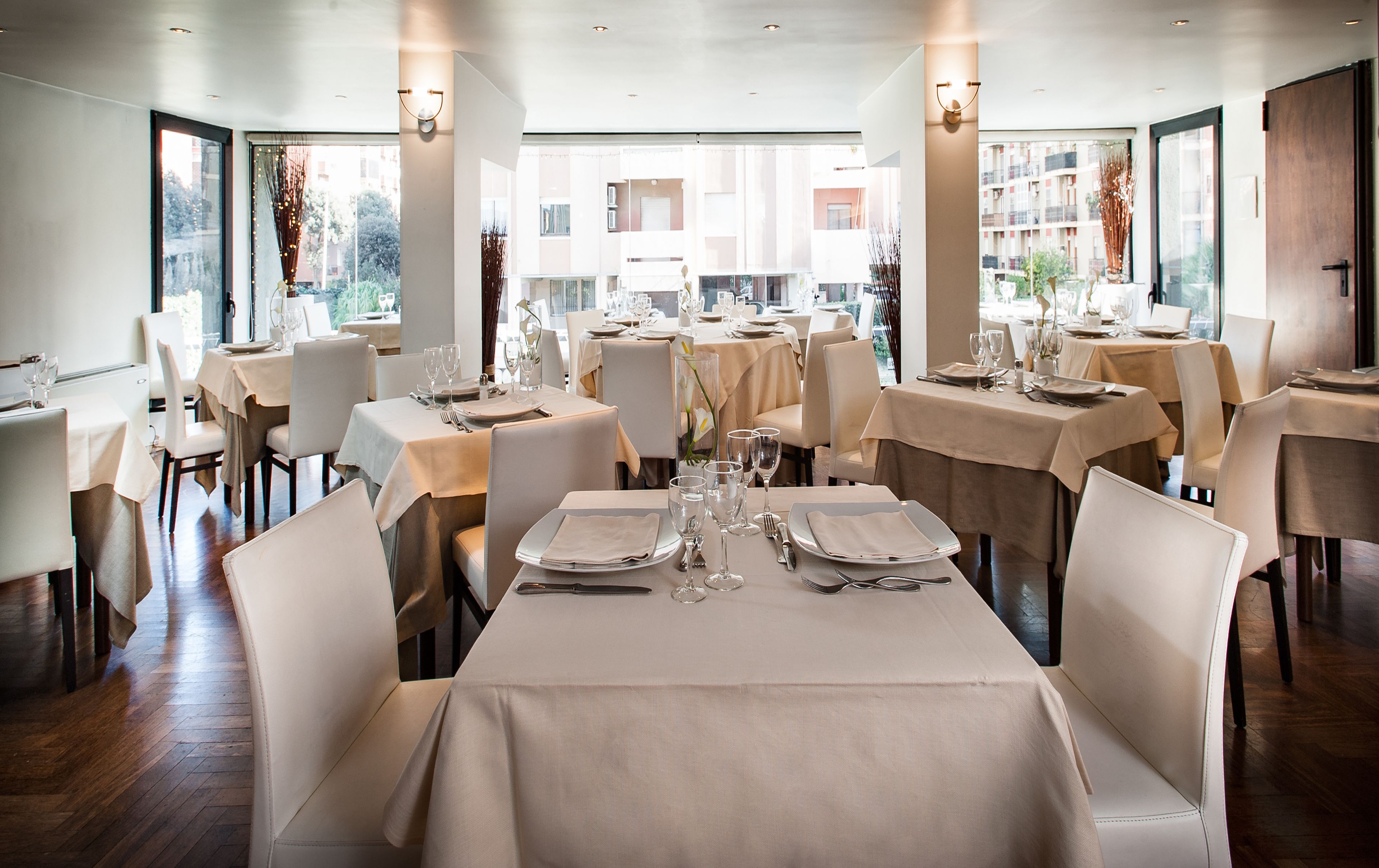 A restaurant with multiple tables set for dining, featuring a modern interior and large windows offering views of the city.