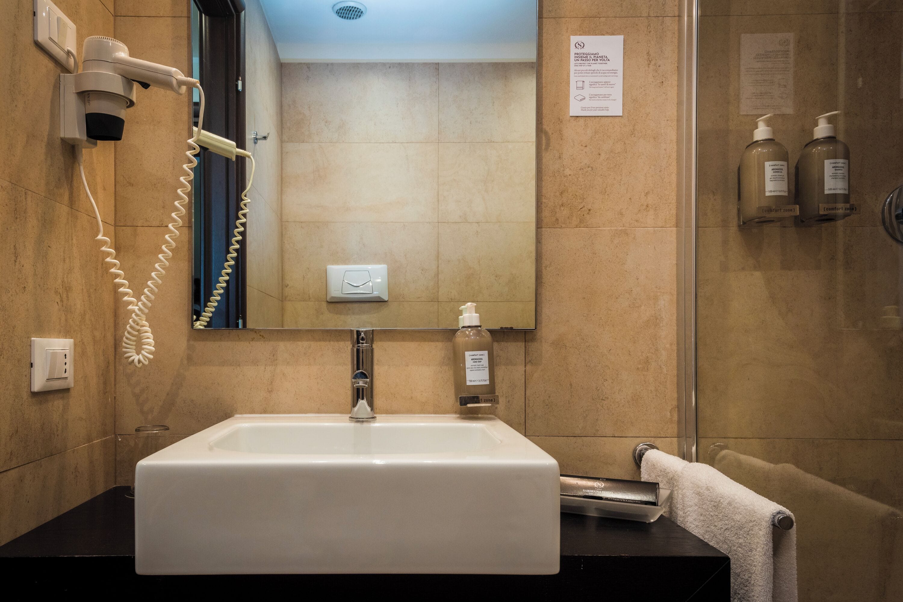 Ein Badezimmer mit einem weißen Waschbecken, einem Fön, einem Spiegel und einem Handtuchhalter.