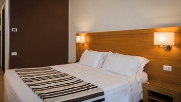 A hotel room with a large bed, a wooden headboard, two bedside lamps, and a bedside table.