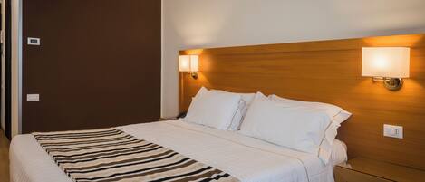 A hotel room with a large bed, a wooden headboard, two bedside lamps, and a bedside table.
