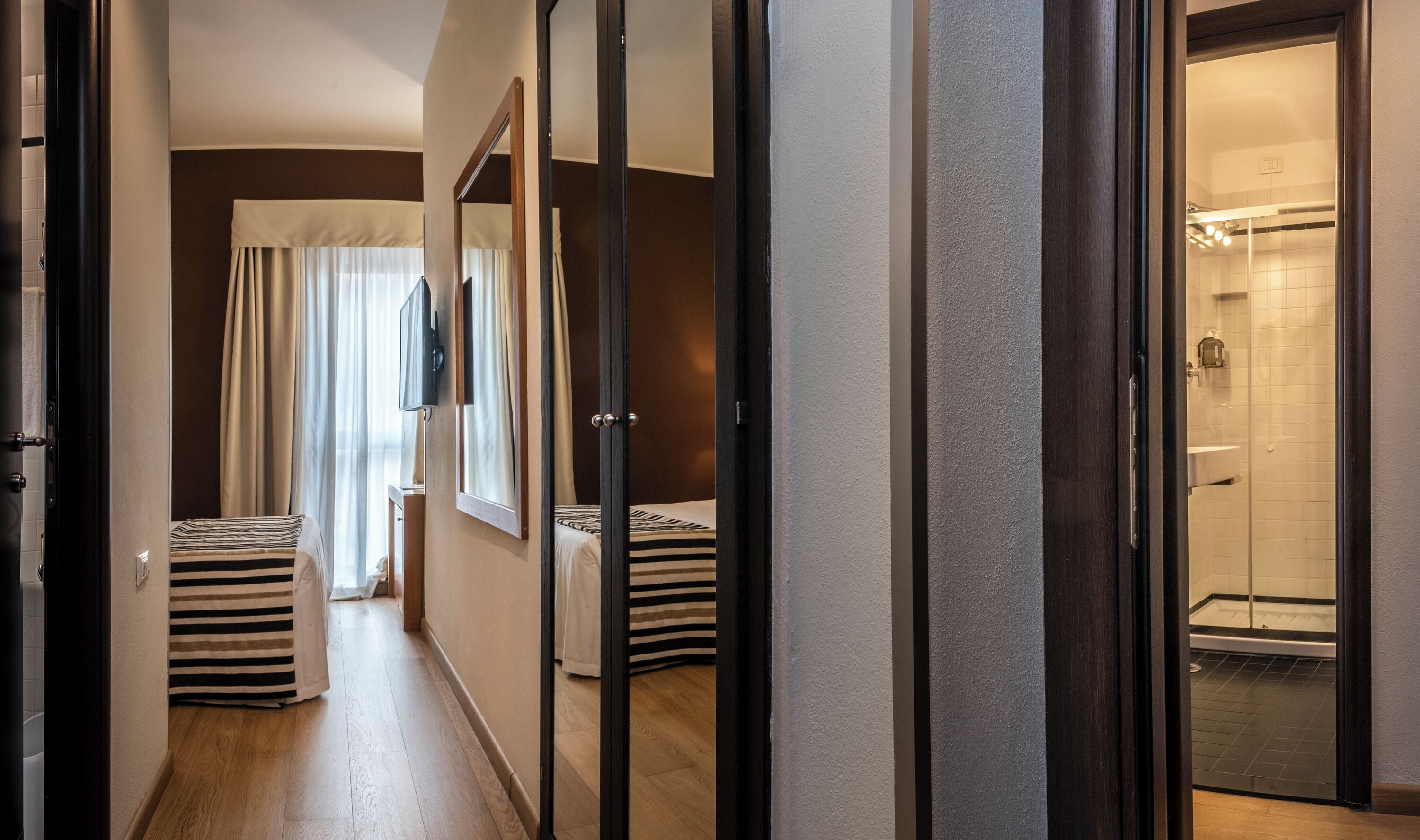 A hotel hallway with a bed, a bathroom, and a shower area.