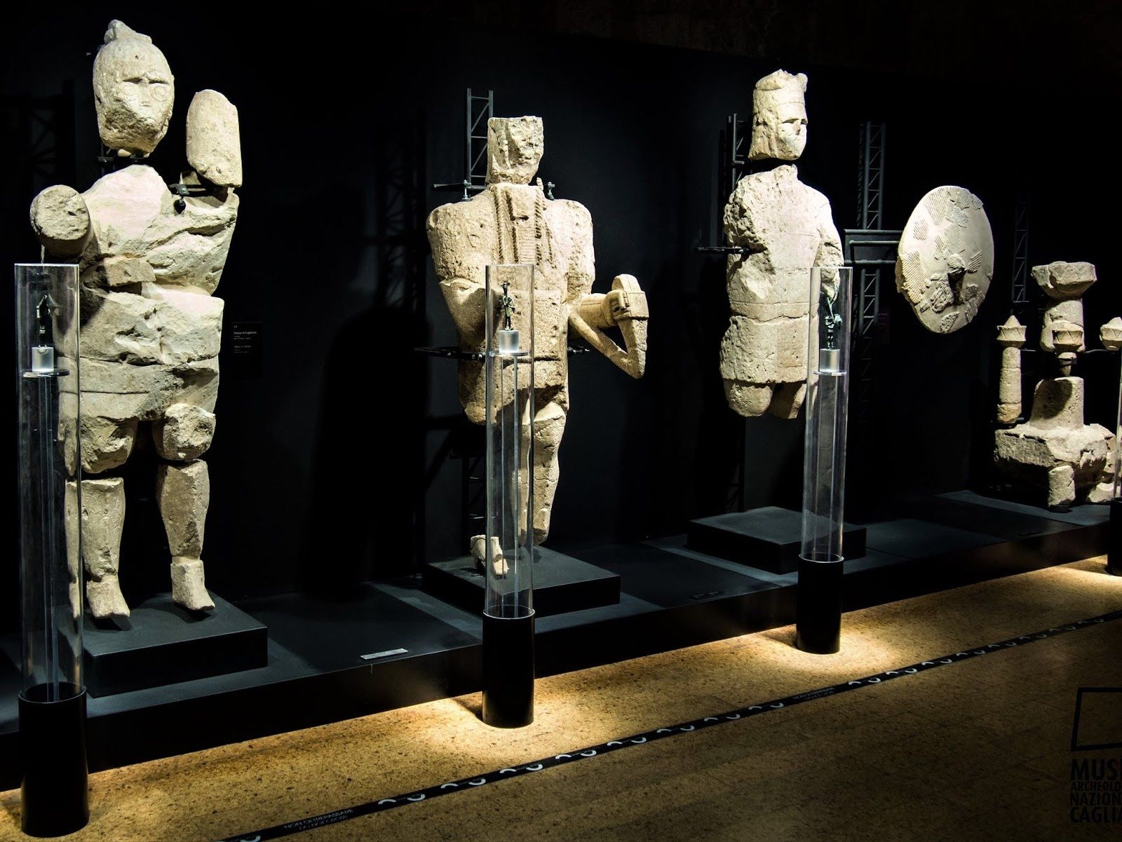 Una exhibición de museo con antiguas esculturas de piedra en vitrinas de cristal.