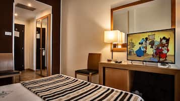 Ein Hotelzimmer mit einem Bett, einem Schreibtisch mit Lampe, einem Fernseher, der animierte Figuren zeigt, und einem Sessel.