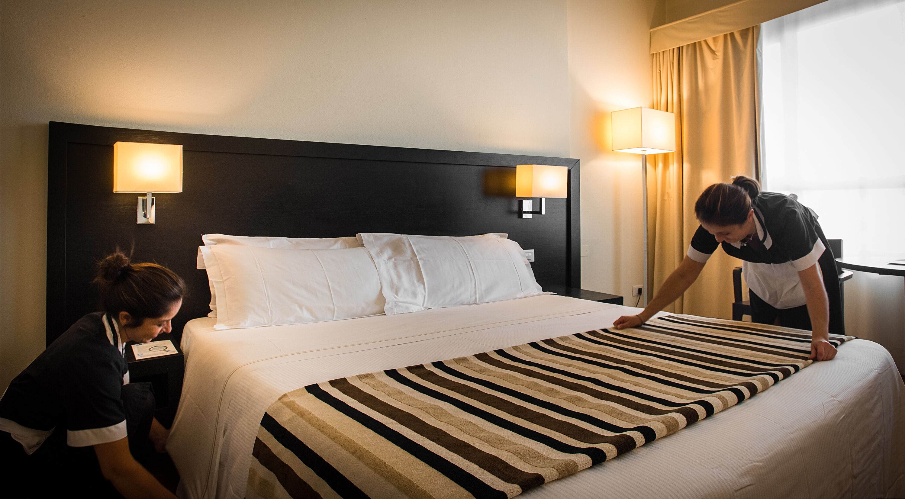 Habitación de hotel con cama, dos lámparas de noche y una ventana con cortinas.