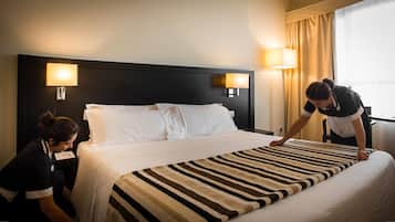 Habitación de hotel con cama, dos lámparas de noche y una ventana con cortinas.