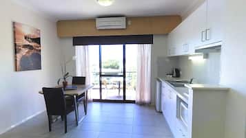 A compact kitchen with white cabinets, a dining area with a table and chairs, and a view of a balcony with outdoor furniture.